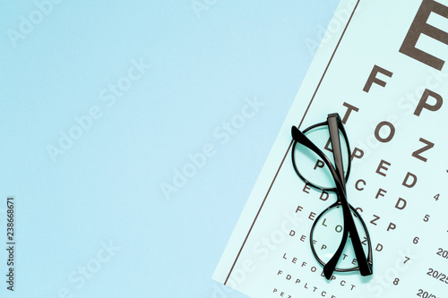 Eye test, eye examination. Glasses with transparent optical lenses on eye test chart on blue background top view