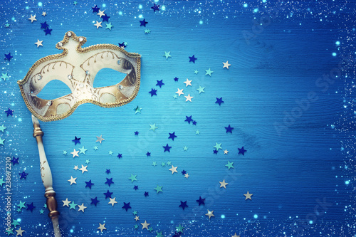 carnival party celebration concept with elegant gold mask on stick over blue wooden background and stars. Top view.