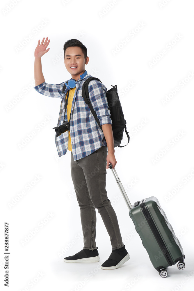 Happy young Asian man with luggage waving at camera Happy young Asian man with luggage waving at camera