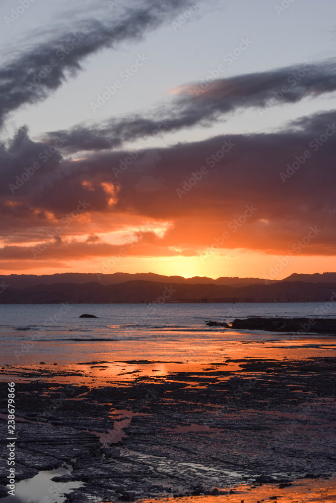 A peach colored sunset reflected in the beach rock pools at Gisborne, New Zealand.