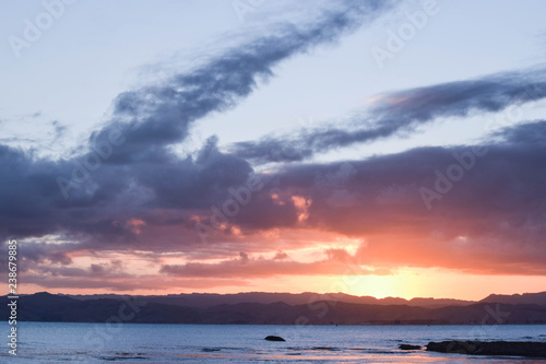 A pale sunset in a light blue sky filled with clear cloud shapes above the beach in Gisborne  New Zealand.