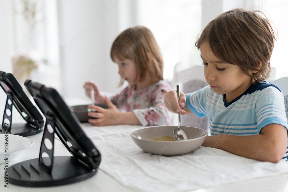 Kids in dining room eating and watching tablet Kids in dining room eating and watching tablet