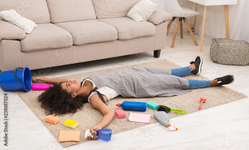 Tired woman with cleaning supplies lying on floor