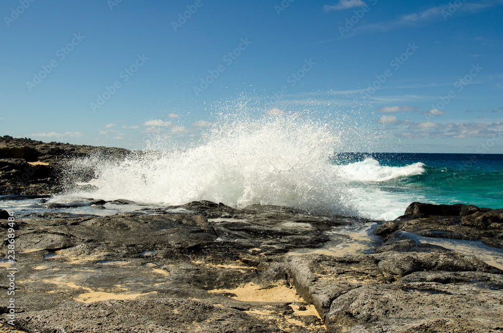 Adventure on the rocky coast near Playa de la Conchas beach on La Graciosa island, Canary Islands, Atlantic ocean, the strong waves are spreading over the rocks. Adventure on the rocky coast near Playa de la Conchas beach on La Graciosa island, Canary Islands, Atlantic ocean, the strong waves are spreading over the rocks.