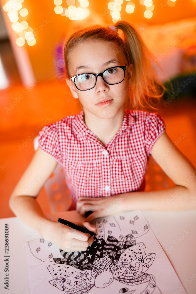 Blonde girl in the pink dress and big black glasses drawing santa claus. Christmas and New Year theme, yellow bokeh