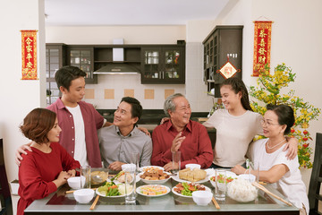 Big Vietnamse family enjoying traditional dinner and celebrating Lunar New Year, couplets with best wishes for coming year in the background