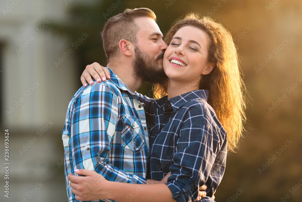 Handsome man kissing tenderly his girlfriend in cheek outdoors Handsome man kissing tenderly his girlfriend in cheek outdoors