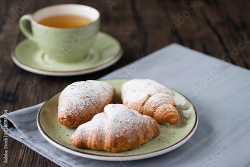 Freshly baked croissants cup with green tea on a brown wooden background.