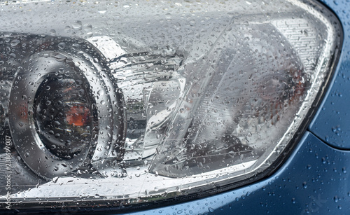 Raindrops on part of the headlight and body of metallic blue car after rain shower.