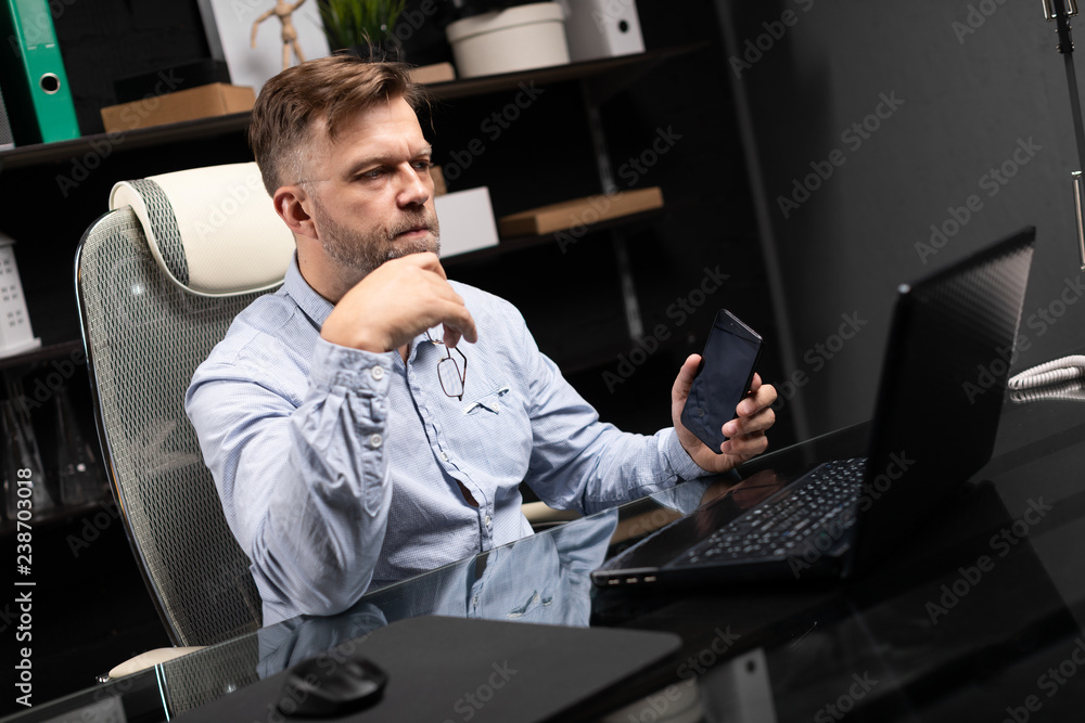 Serious businessman working on a laptop and talking on a mobile phone Serious businessman working on a laptop and talking on a mobile phone