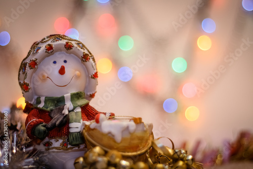 snowman close-up on the background of blurry colored lights tinsel and Happy New Year.