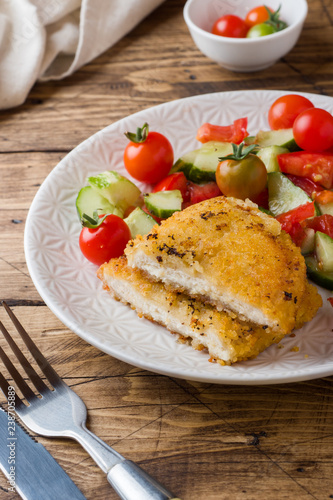 Chicken cutlet and cucumber salad with tomatoes on a wooden table