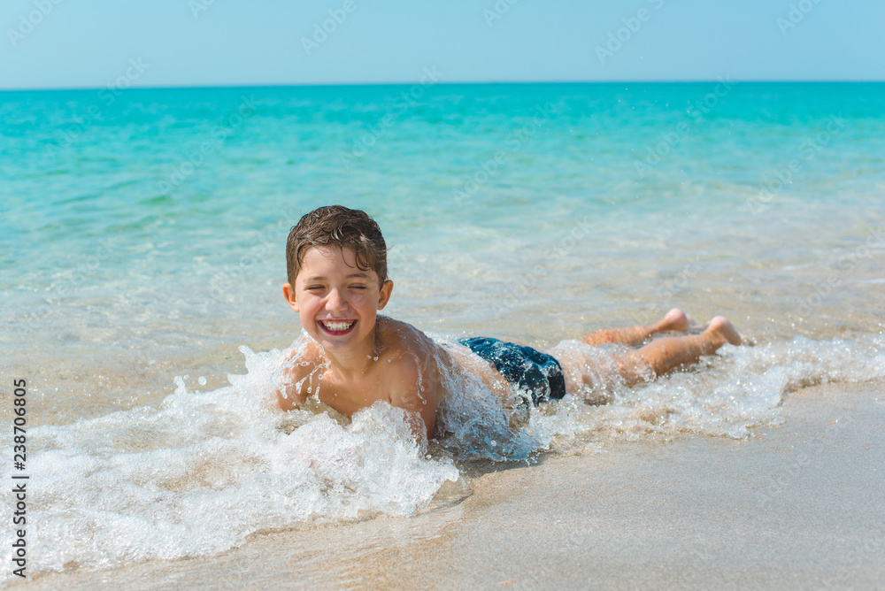 A cheerful kid on the beach lies in the clear sea water.