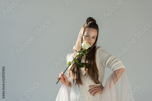 Foto attractive woman in fashionable winter outfit sniffing white rose and looking at