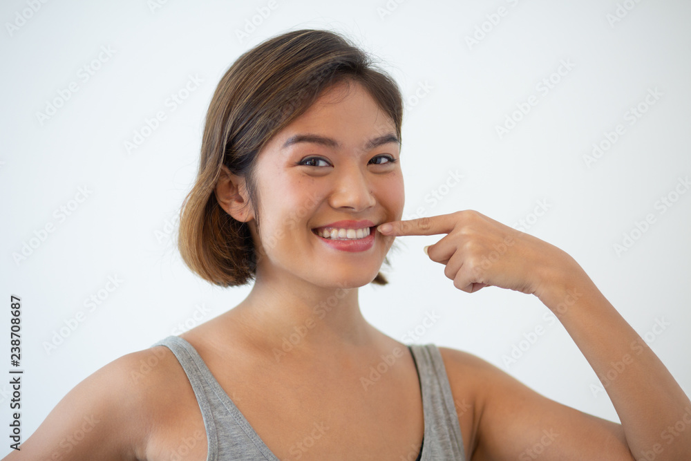 Smiling beautiful Asian woman pointing at her teeth. Young woman showing teeth and looking at camera. Teeth hygiene and whitening concept. Isolated view on white background. Smiling beautiful Asian woman pointing at her teeth. Young woman showing teeth and looking at camera. Teeth hygiene and whitening concept. Isolated view on white background.