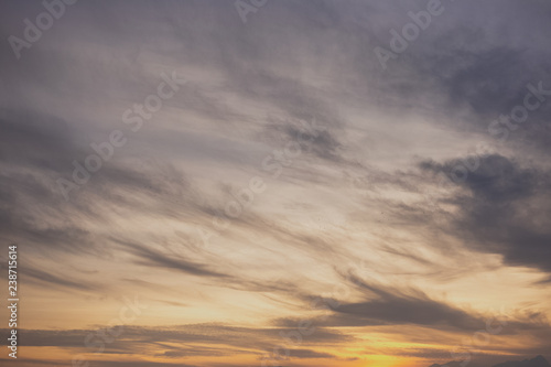 Sunset charming sky background with soft calm white clouds and evening sunlight. Beautiful nature background. Horizontal color photography.