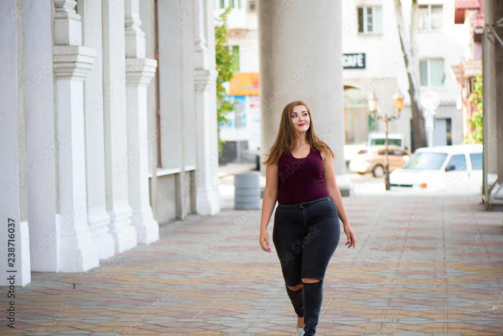 Fototapeta premium Pretty young woman walking on the city street. Casual fashion, plus size model. xxl women on nature.