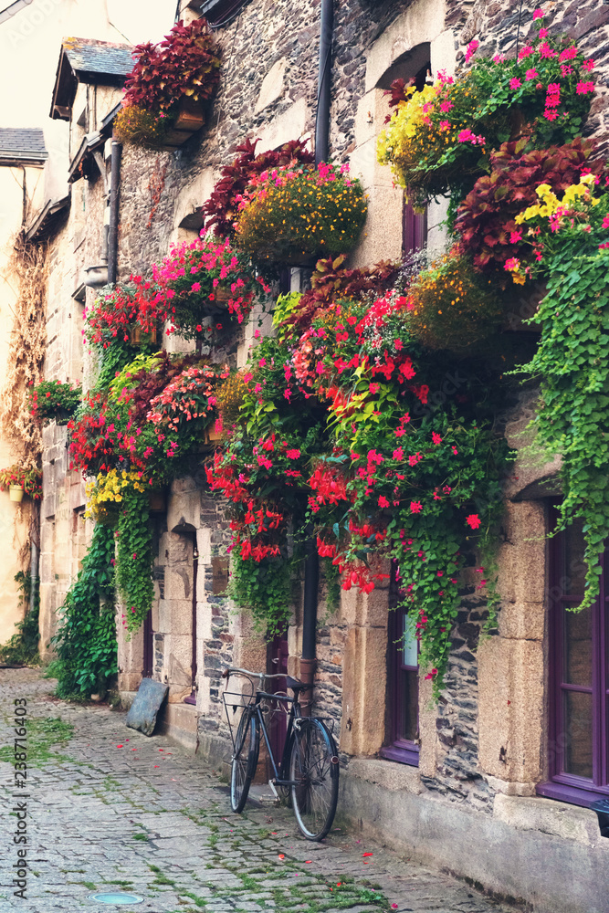 Vintage bicycle in front of the old rustic house, covered with flowers. Beautiful city landscape with an old bike near the stone wall with flowers in drawers in France, Europe. Retro style.