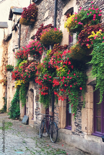 Fototapeta Naklejka Na Ścianę i Meble -  Vintage bicycle in front of the old rustic house, covered with flowers. Beautiful city landscape with an old bike near the stone wall with flowers in drawers in France, Europe. Retro style.