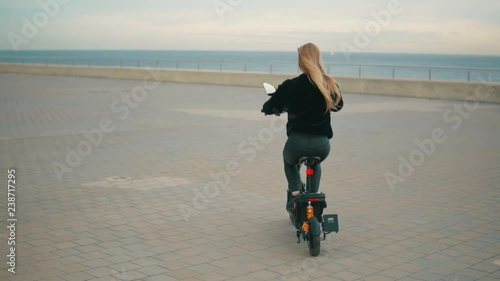 Pretty blonde woman driving electric bike near sea. Modern city transportation photo