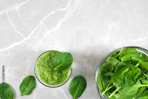 Green healthy spinach smoothie in a  glass, bowl with fresh spinach and spinach leaves on a marble background with copy space.