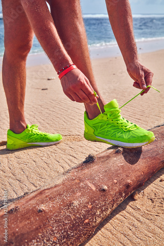 Man tying running sneakers on a tropical exotic beach.