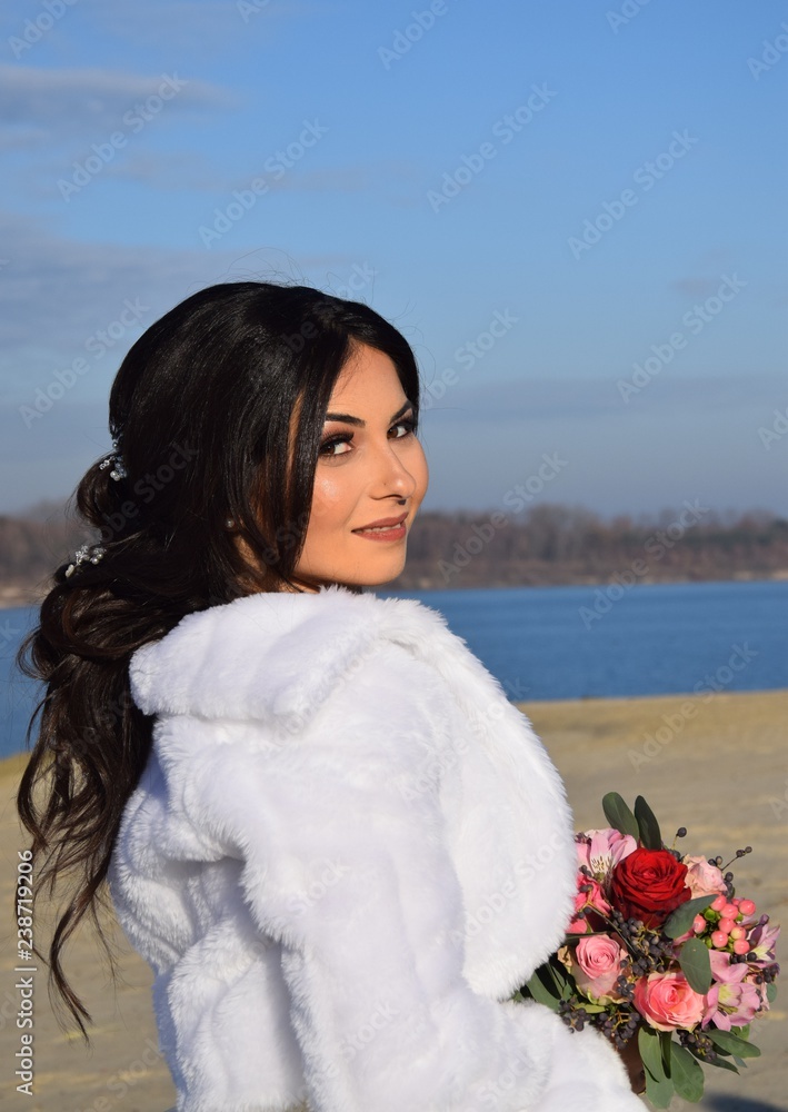 Wunderschöne Braut in einem weißen Brautkleid, Schleier, und Blumenstrauß an einem Strand bei blauem Himmel im Sommer Wunderschöne Braut in einem weißen Brautkleid, Schleier, und Blumenstrauß an einem Strand bei blauem Himmel im Sommer