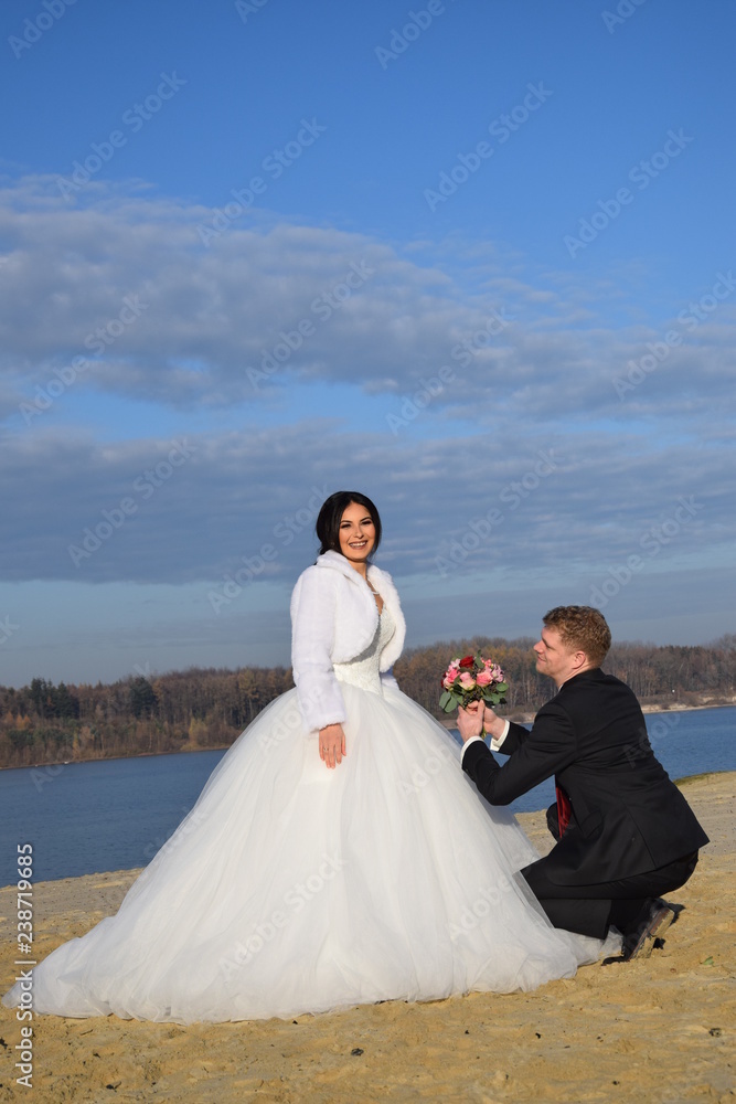 Bräutigam kniet mit Blumenstrauß vor seiner Braut am Strand