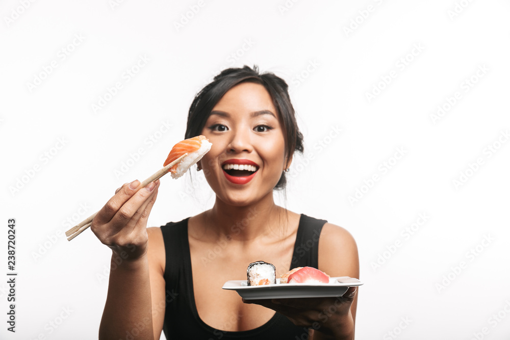 Cheerful young asian woman eating sushi with chopsticks Cheerful young asian woman eating sushi with chopsticks