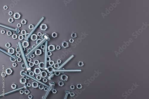 Metal nuts and bolts scattered on a grey background