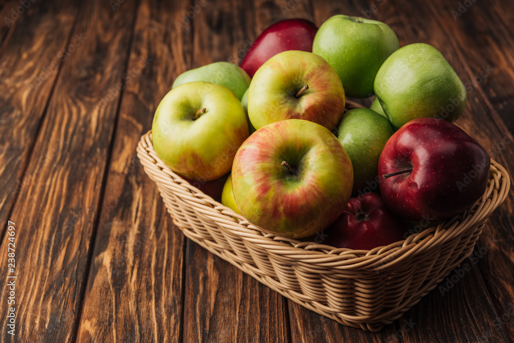 ripe multicolored apples in wicker basket on rustic wooden table ripe multicolored apples in wicker basket on rustic wooden table