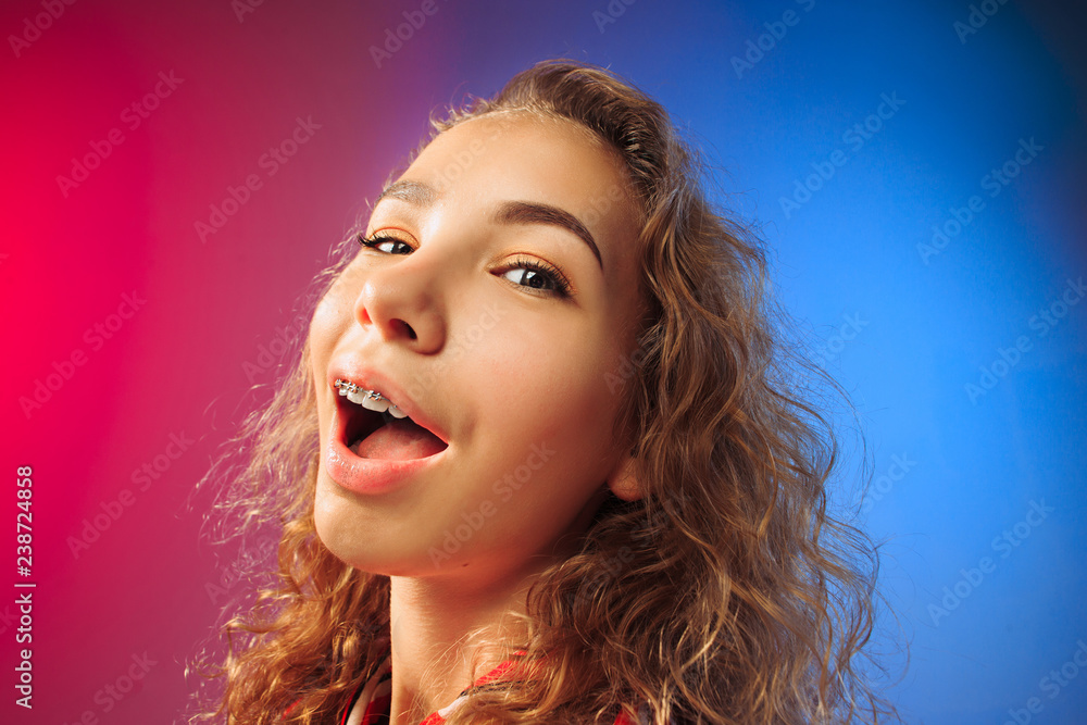 Fototapeta premium Happy business woman standing and smiling on red and blue studio background. Beautiful female half-length portrait. Young emotional woman. The human emotions, facial expression concept