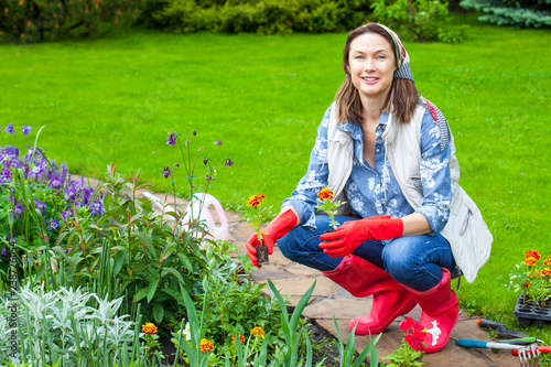 Tableau sur toile smiling woman in kerchief and red boots planting flowers