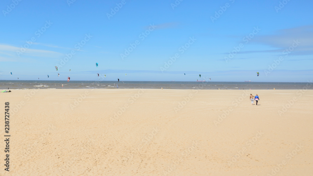 Breiter Sandstrand an der Nordseeküste in Scheveningen bei Den Haag, Niederlande - mit Kites von Kitesurfern am Horizont