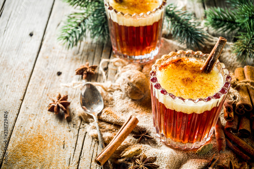 Winter holidays traditional drink, homemade hot buttered rum with spices, over old rustic wooden background with christmas tree branches, copy space