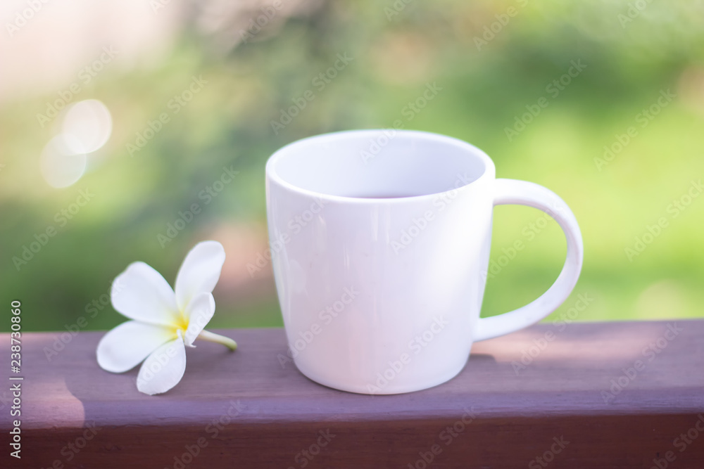 Selective focus white coffee mug and flower are placed on wooden floor with blurred background.