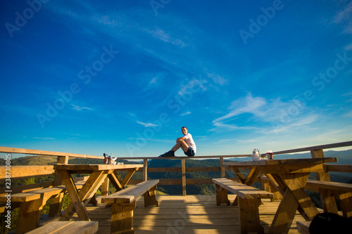 Young man sits in open air cafe with terrace and enjoy beautiful view of mountains