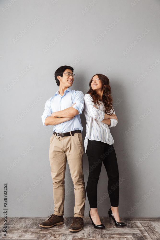 Full length of cheerful asian couple standing back to back Full length of cheerful asian couple standing back to back