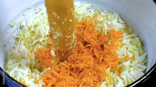 Cooking sauerkraut in an enamelled bucket. Squeezing the juice out of vegetables using a wooden pestle. photo