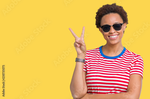 Beautiful young african american woman wearing sunglasses over isolated background smiling with happy face winking at the camera doing victory sign. Number two.