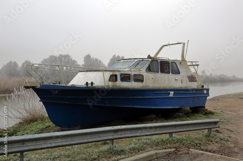 White-blue abandoned rusty boat on the banks of a misty river