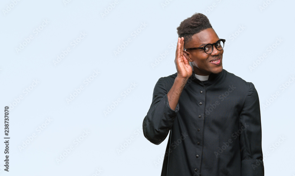 Young african american priest man over isolated background smiling with hand over ear listening an hearing to rumor or gossip. Deafness concept. Young african american priest man over isolated background smiling with hand over ear listening an hearing to rumor or gossip. Deafness concept.