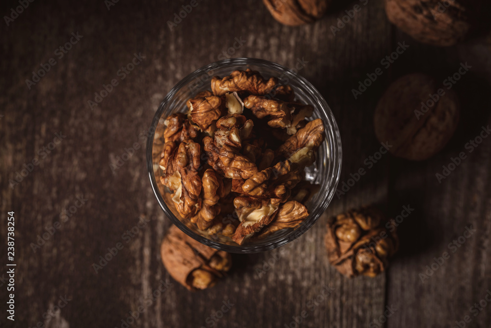 top view of shelled walnuts in glass on wooden backdrop top view of shelled walnuts in glass on wooden backdrop