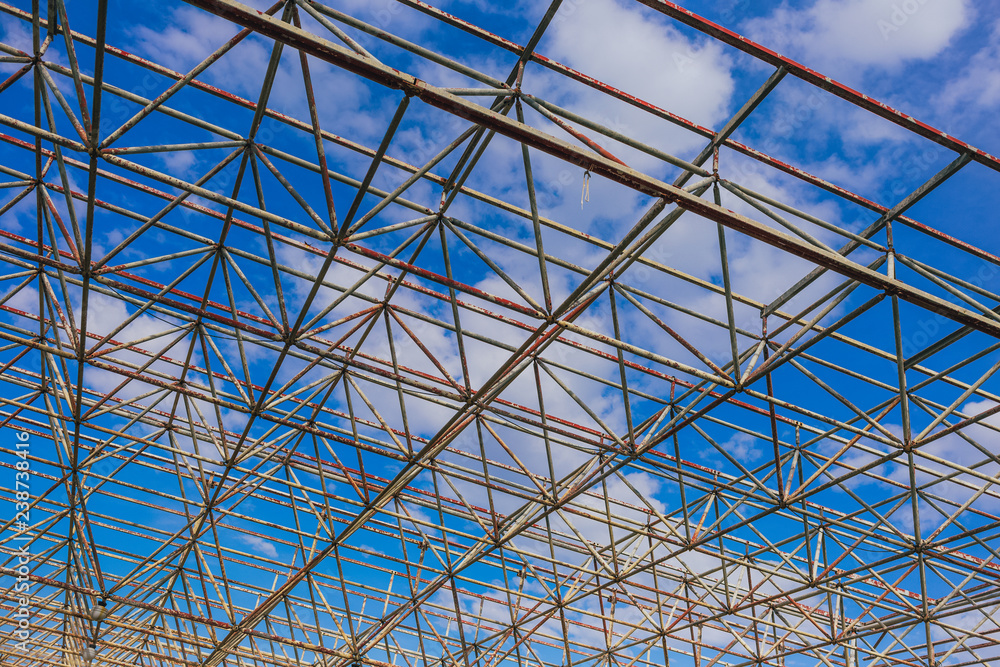 Urban abstract texture background. Point of view looking up in blue sky through old rusty geometric diagonal metal constructions of abandoned building. Horizontal color photography.