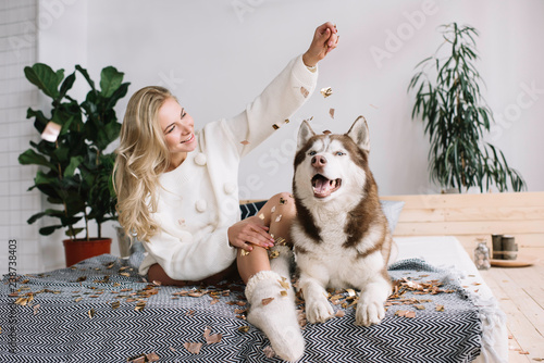 Happy girl and husky sitting on the bed at cozy home. Sexy woman beautiful  body and long legs celebration success. Party time. Elegant smiling female  playing with cute adorable dog in bedroom.