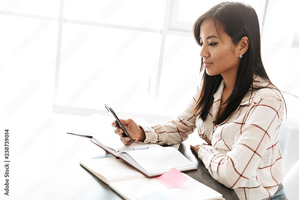 Image of asian businesswoman 20s working with documents, while sitting at table indoor Image of asian businesswoman 20s working with documents, while sitting at table indoor