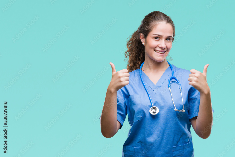 Young brunette doctor girl wearing nurse or surgeon uniform over isolated background success sign doing positive gesture with hand, thumbs up smiling and happy. Looking at the camera Young brunette doctor girl wearing nurse or surgeon uniform over isolated background success sign doing positive gesture with hand, thumbs up smiling and happy. Looking at the camera