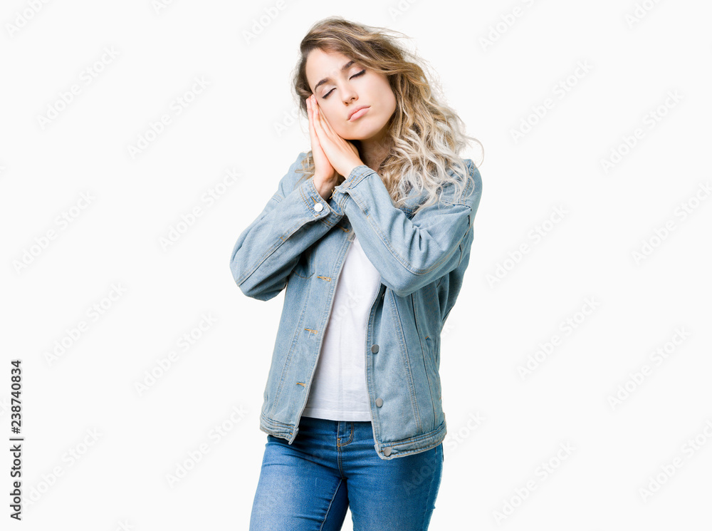 Beautiful young blonde woman wearing denim jacket over isolated background sleeping tired dreaming and posing with hands together while smiling with closed eyes. Beautiful young blonde woman wearing denim jacket over isolated background sleeping tired dreaming and posing with hands together while smiling with closed eyes.