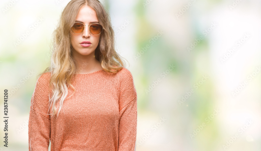 Beautiful young blonde woman wearing sunglasses over isolated background with serious expression on face. Simple and natural looking at the camera. Beautiful young blonde woman wearing sunglasses over isolated background with serious expression on face. Simple and natural looking at the camera.
