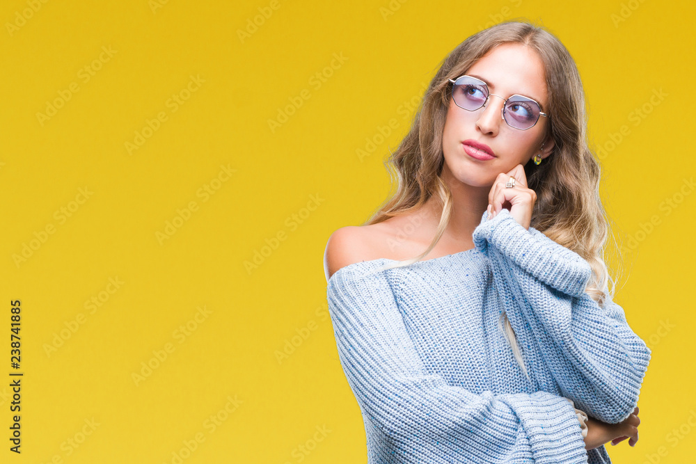 Beautiful young blonde woman wearing sunglasses over isolated background with hand on chin thinking about question, pensive expression. Smiling with thoughtful face. Doubt concept. Beautiful young blonde woman wearing sunglasses over isolated background with hand on chin thinking about question, pensive expression. Smiling with thoughtful face. Doubt concept.